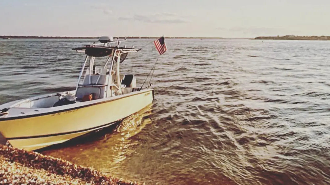American boat flag flying on a small white fishing boat docked along a rocky shoreline at sunset