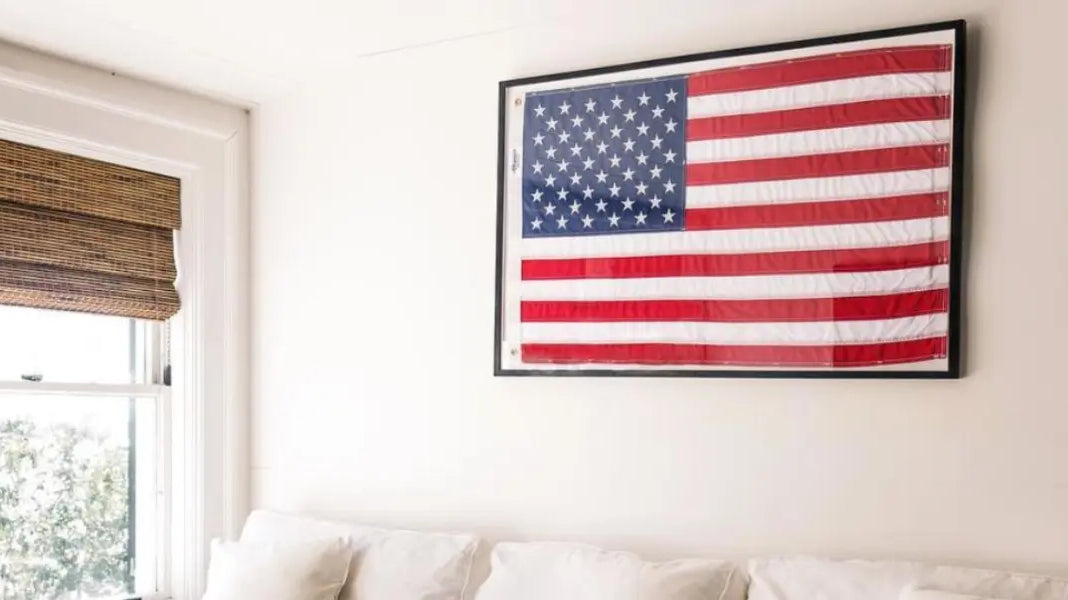 American flag displayed in a black frame above a white couch against a bright cream living room wall