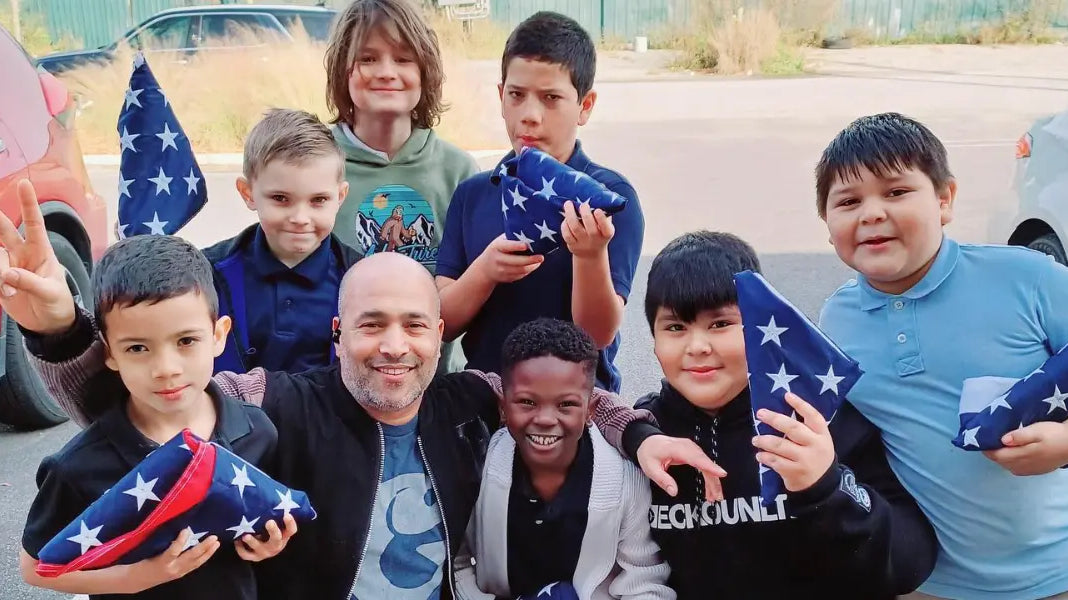 American flag held by smiling children and an adult posing together in a parking lot with folded flags