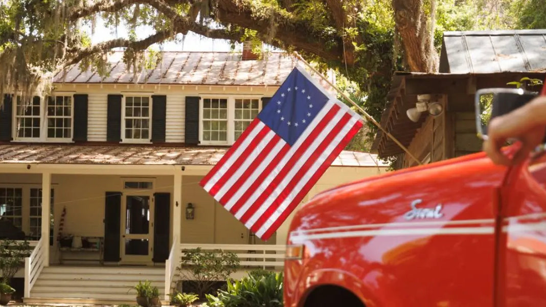 American flag display featuring a Betsy Ross flag mounted on a porch of a classic white house with black shutters