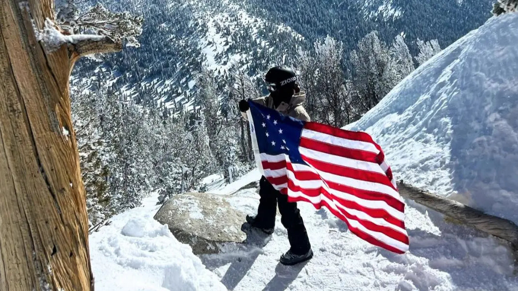 American flag etiquette followed as a hiker holds the flag respectfully on a snowy mountain trail.