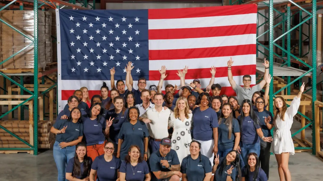 Employees of an American flag store gathered in front of a massive U.S. flag inside their warehouse