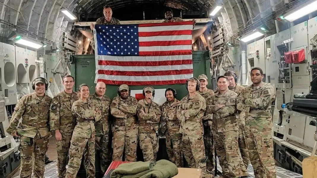 American flag veterans posing proudly in uniform beneath a large American flag inside a military aircraft