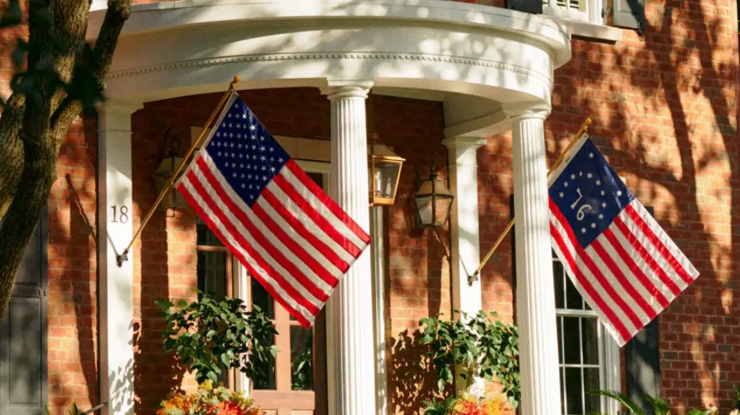 American revolutionary war flags displayed on a brick home with white columns and seasonal decorations.