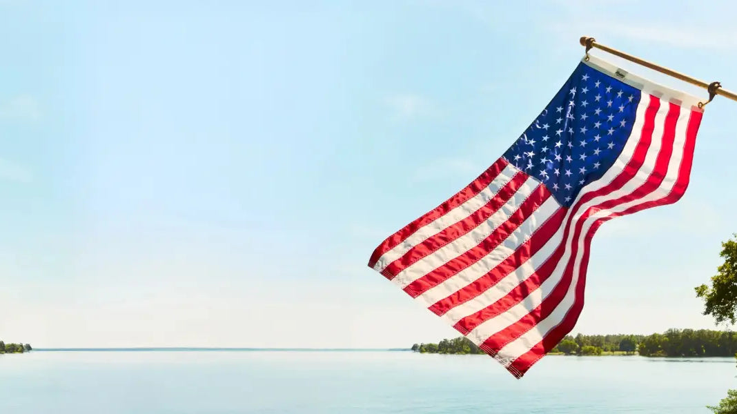 American yard flags waving over a calm lake with a clear blue sky in the background.