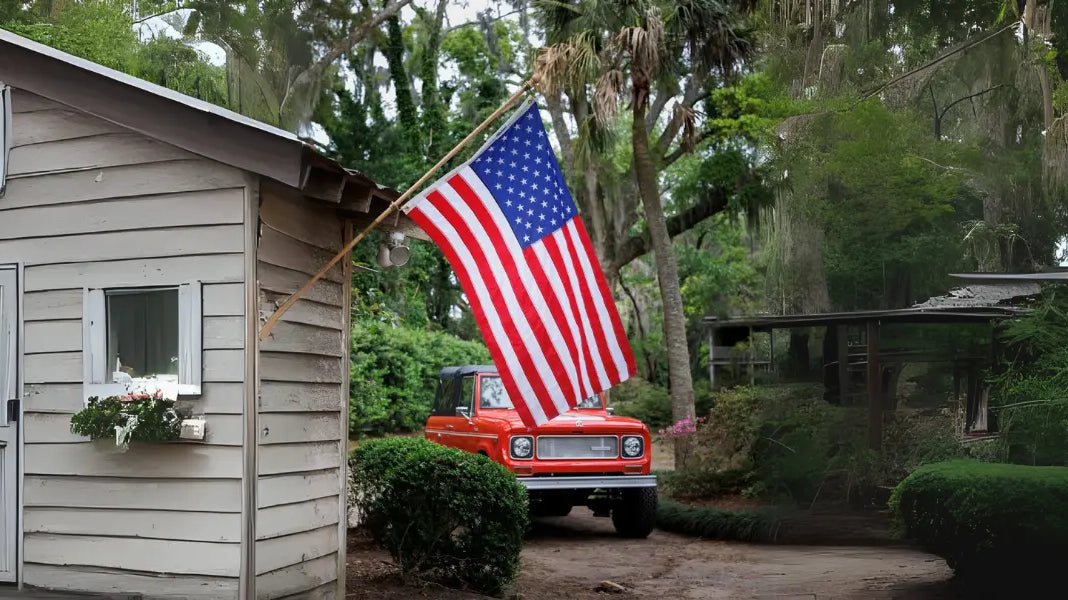 Outdoor American flag hangs beside a rustic cottage with a red truck in a wooded yard.