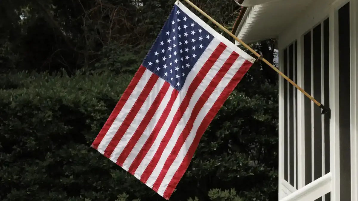 American flag mounted on a white porch with greenery in the background.