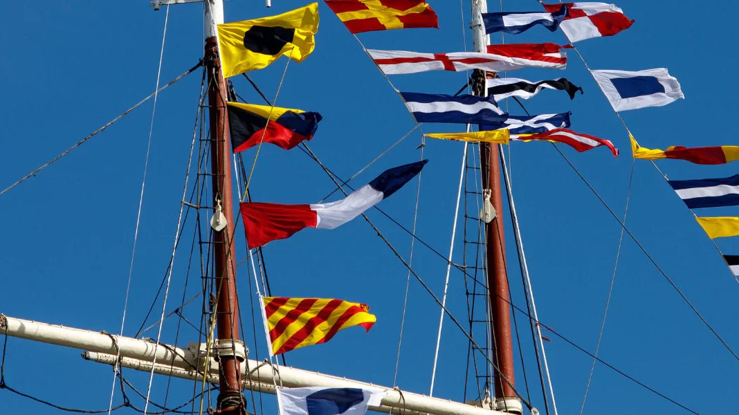 Maritime signal flags flying on a ship mast against a clear blue sky.