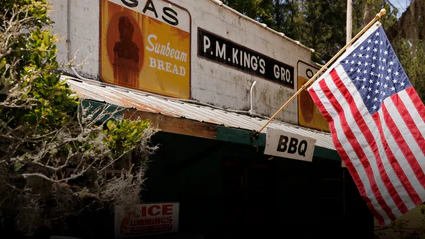Durable American flag waving outside a rustic BBQ shop, mounted on a sturdy wooden pole