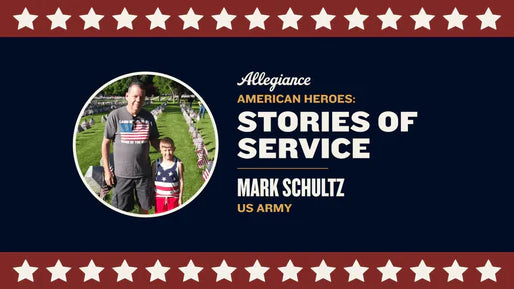 Mark Schultz stands with a young boy dressed in patriotic attire, surrounded by rows of flags in a grassy field