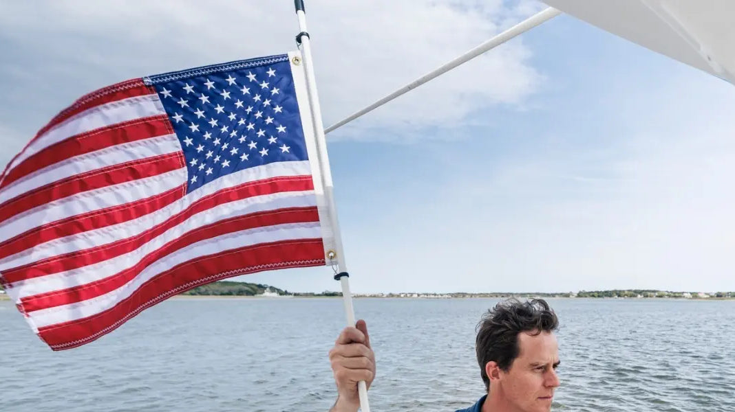 U.S. flag for boats waving from a stern-mounted pole above calm coastal waters under partly cloudy sky