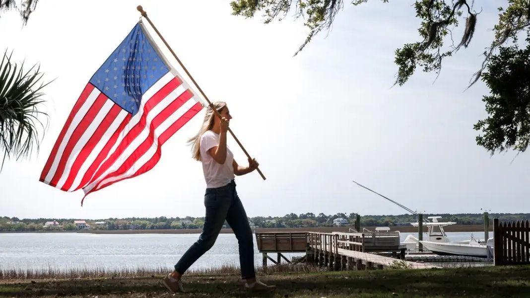 Best American flag waving as a woman walks beside a waterfront dock on a sunny day