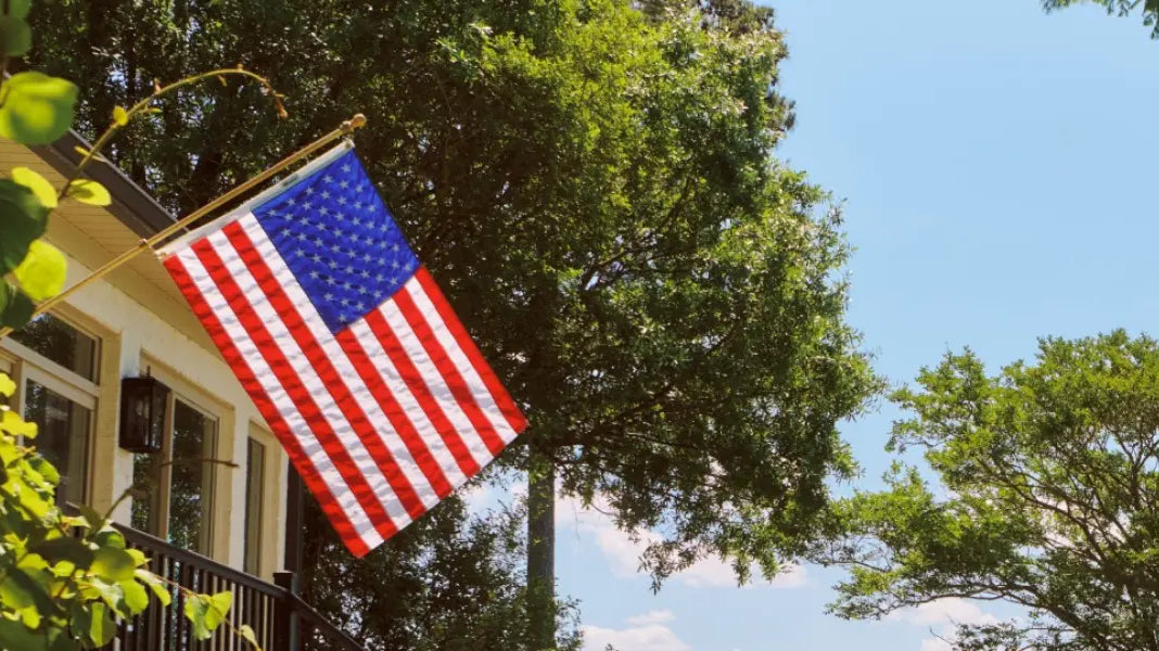 Durable American flag mounted on a home exterior, waving clearly against a bright blue summer sky.