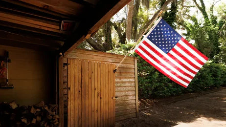 Durable American flag waving outside a rustic wooden shed in a sunlit forest setting