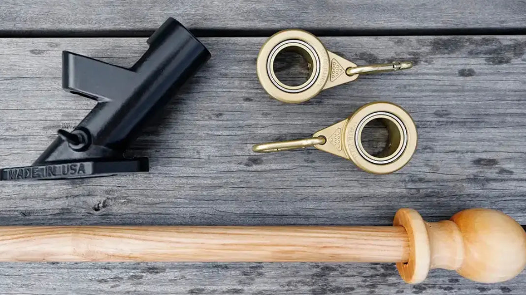 Flagpole installation kit including a black bracket, gold rings, and a wooden pole on a rustic wood surface.