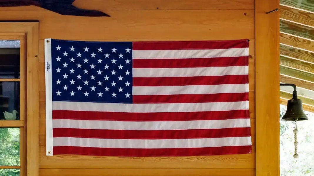 Hand-sewn American flag displayed flat against a wooden wall under a covered porch.