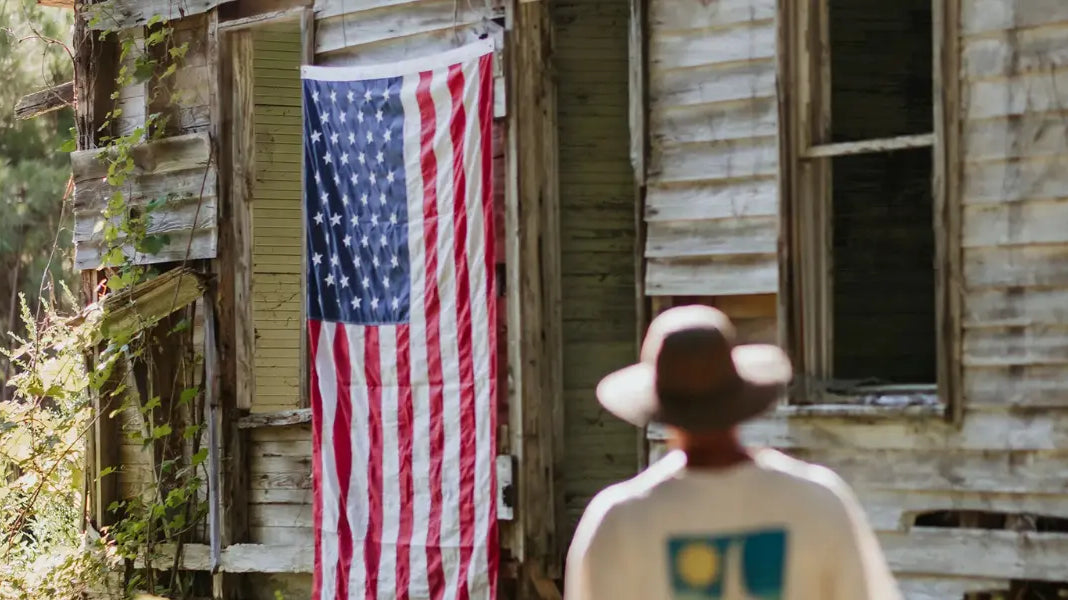 High-quality flags made in the USA hanging on the side of a weathered wooden building with a man in the foreground.