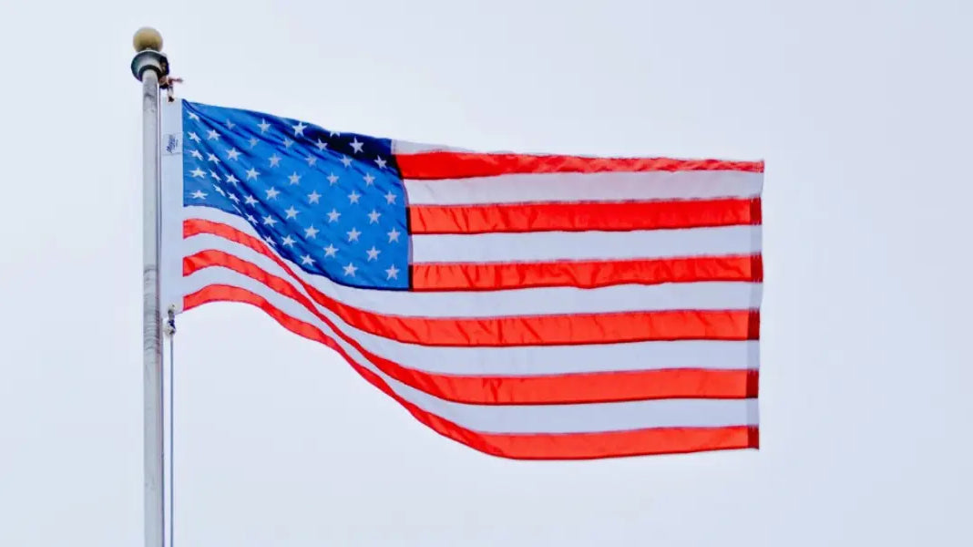 Made-in-USA flag flying on a tall metal pole against an overcast sky.