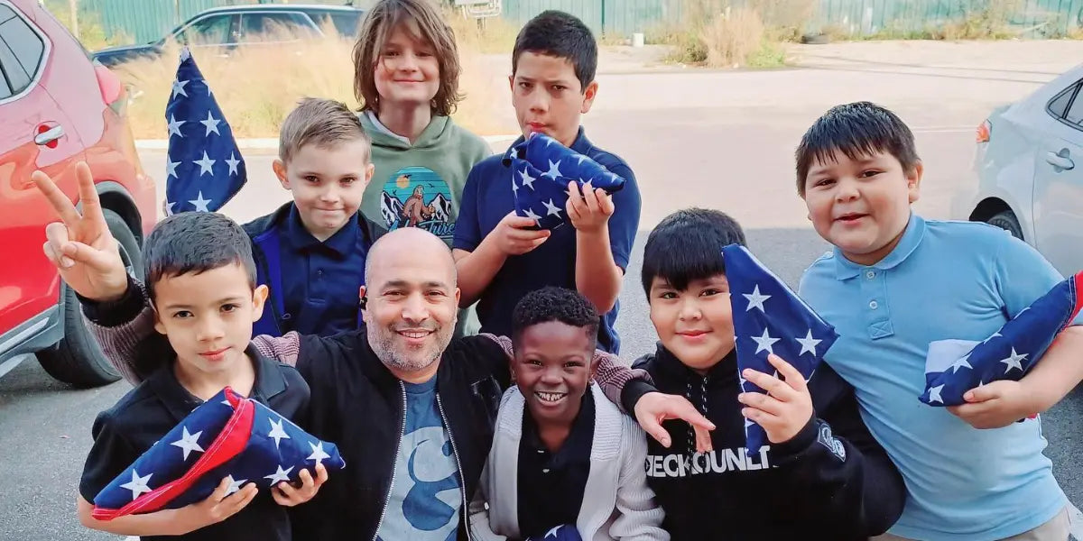 American flag held by smiling children and an adult posing together in a parking lot with folded flags