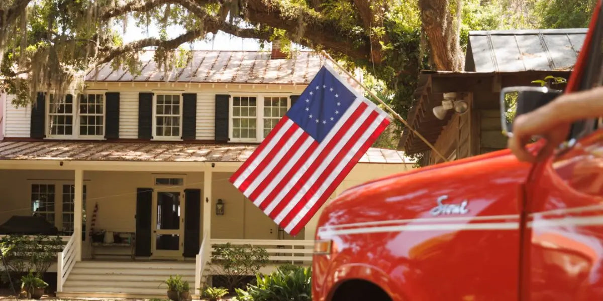 American flag display featuring a Betsy Ross flag mounted on a porch of a classic white house with black shutters
