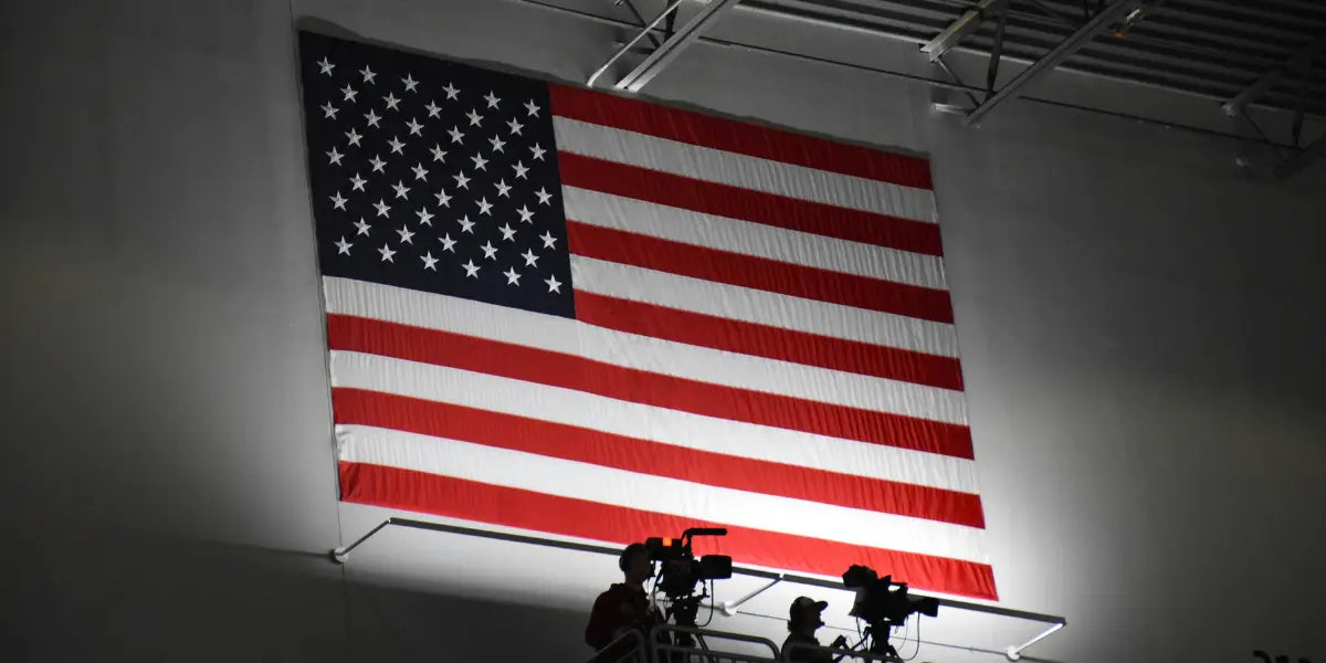 American flag protocol observed with a large illuminated flag hanging indoors above a camera crew during an event