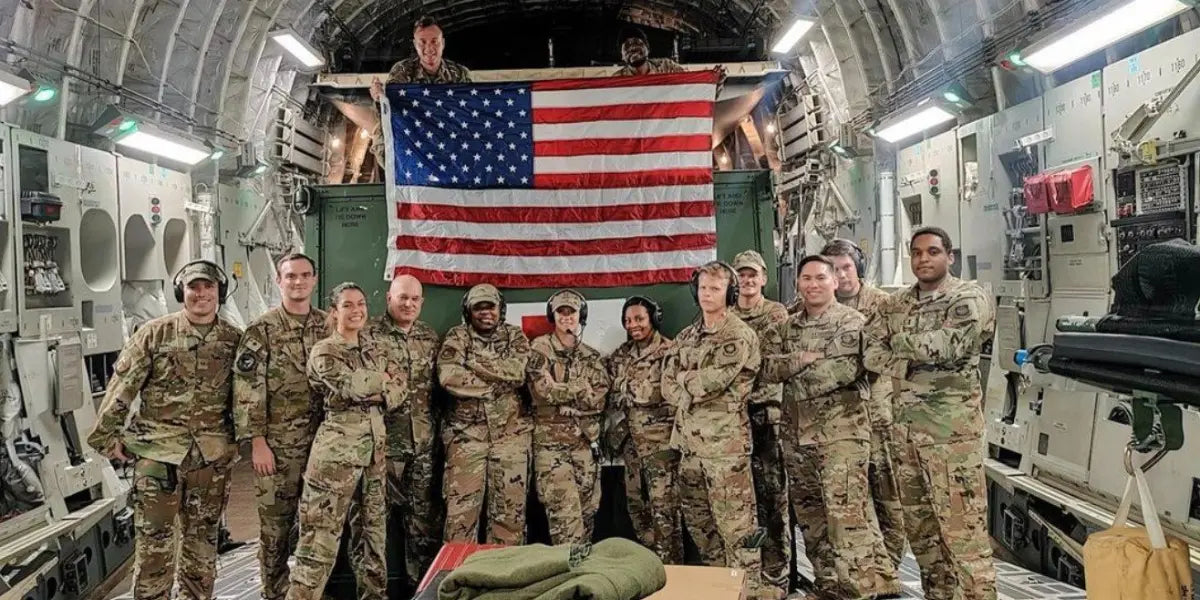 American flag veterans posing proudly in uniform beneath a large American flag inside a military aircraft