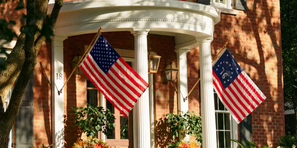 American revolutionary war flags displayed on a brick home with white columns and seasonal decorations.