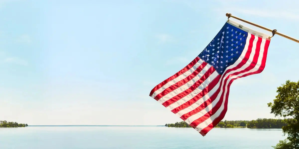 American yard flags waving over a calm lake with a clear blue sky in the background.