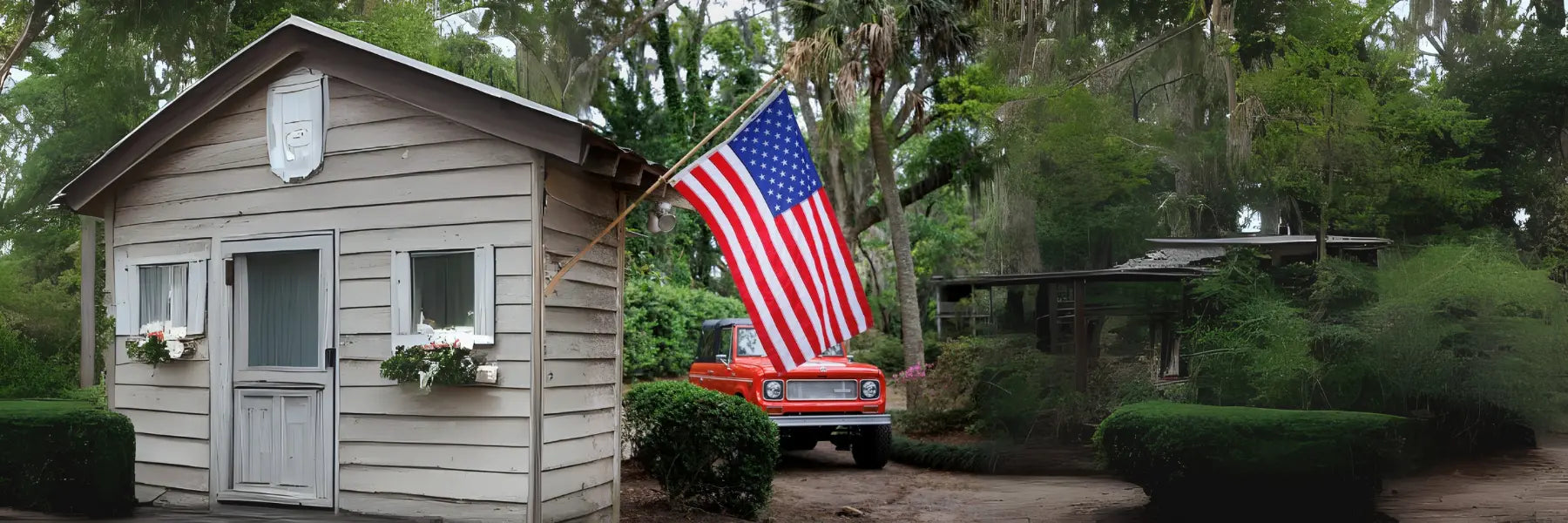 Outdoor American flag hangs beside a rustic cottage with a red truck in a wooded yard.