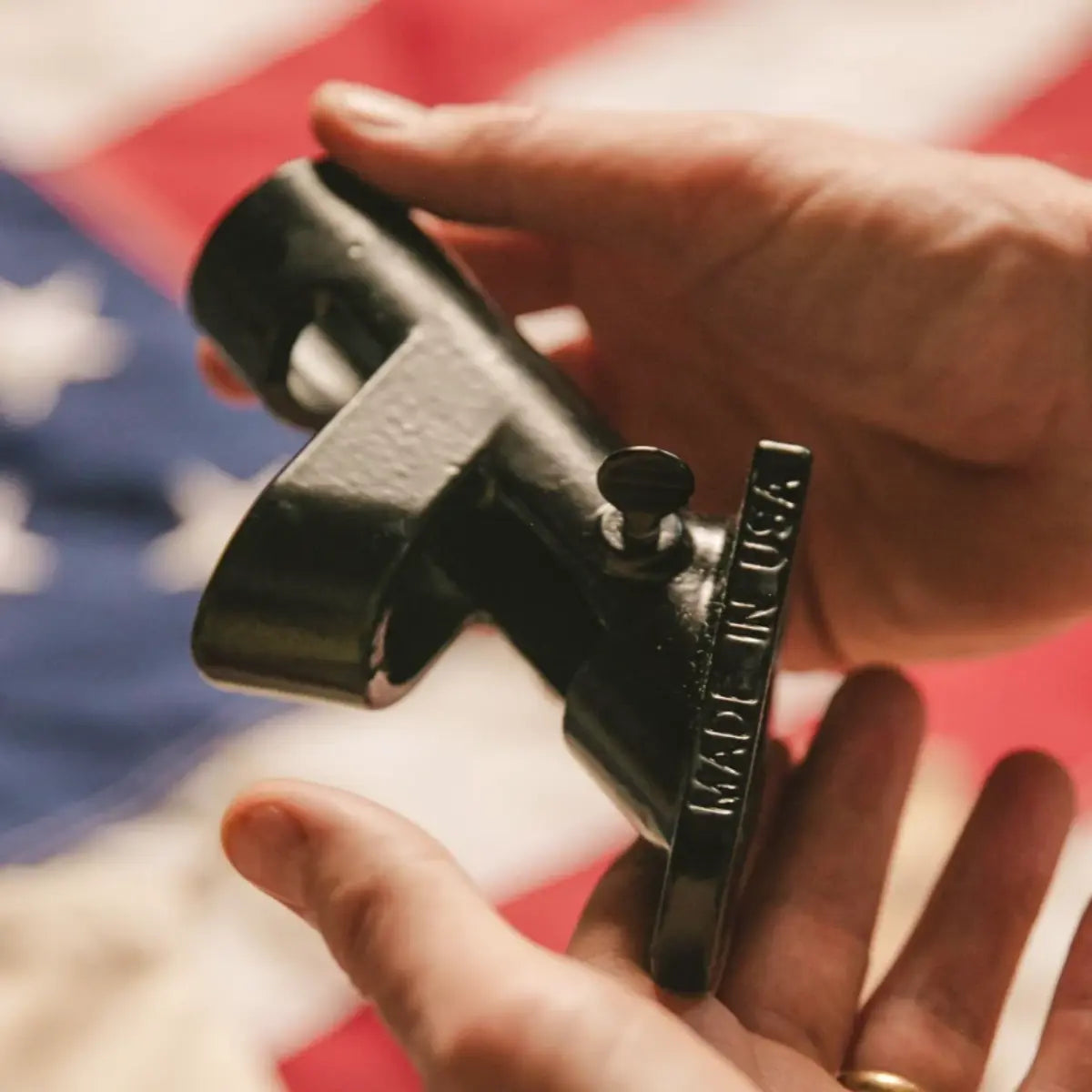 Close-up of hands holding a flagpole for a home stamped with "Made in USA" against an American flag background.