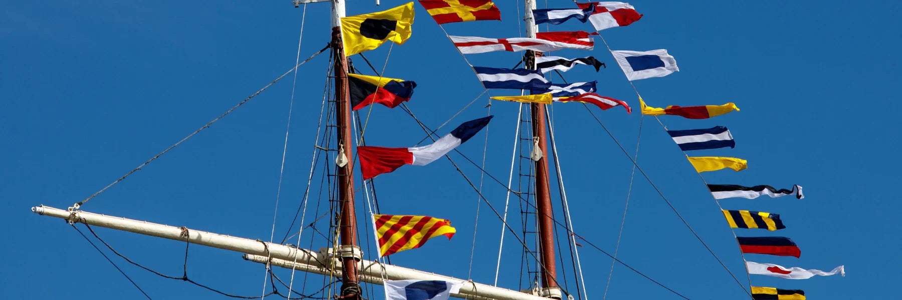 Maritime signal flags flying on a ship mast against a clear blue sky.
