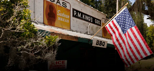 Durable American flag waving outside a rustic BBQ shop, mounted on a sturdy wooden pole