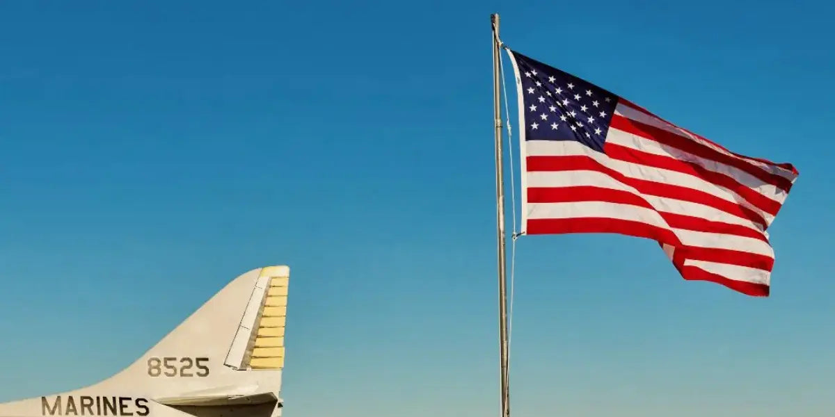 USA flag waving beside a military aircraft tail against a clear blue sky.
