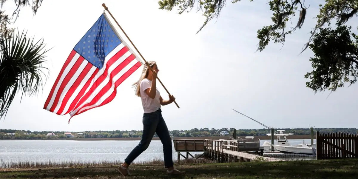 Best American flag waving as a woman walks beside a waterfront dock on a sunny day