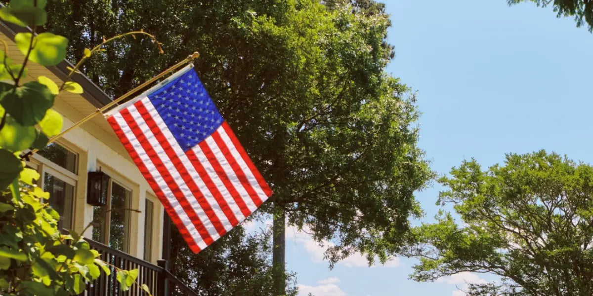 Durable American flag mounted on a home exterior, waving clearly against a bright blue summer sky.