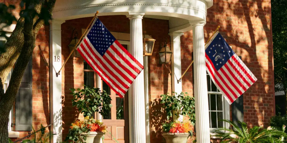 Durable American flags displayed outside a brick home, mounted on poles between tall white columns.
