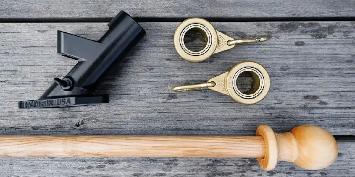 Flagpole installation kit including a black bracket, gold rings, and a wooden pole on a rustic wood surface.