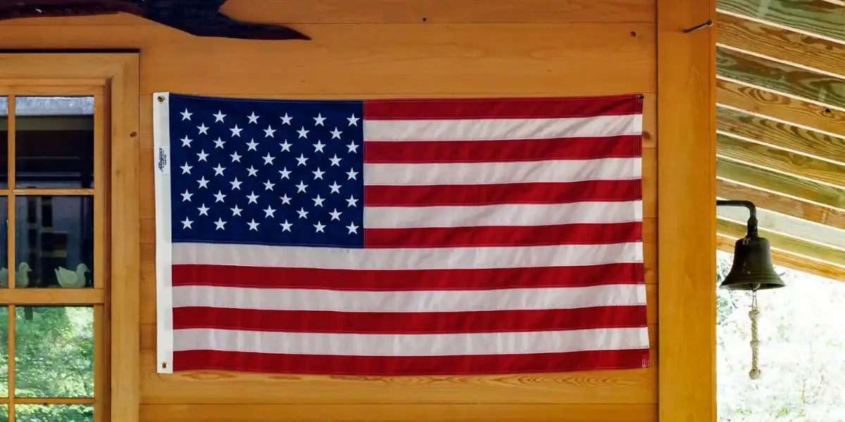 Hand-sewn American flag displayed flat against a wooden wall under a covered porch.