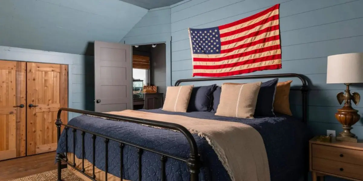 High-quality American flag hanging above a rustic metal bed in a cozy, blue-paneled bedroom.