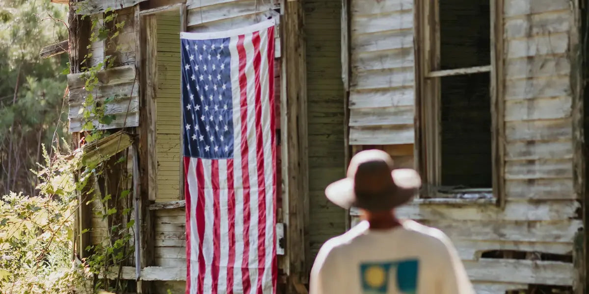 High-quality flags made in the USA hanging on the side of a weathered wooden building with a man in the foreground.