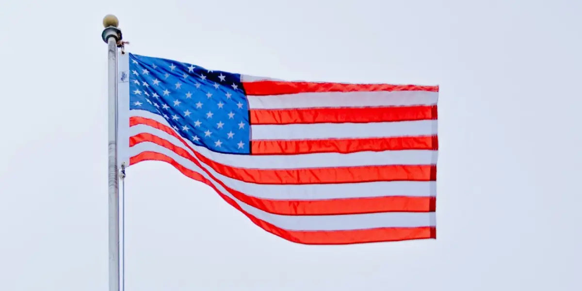 Made-in-USA flag flying on a tall metal pole against an overcast sky.