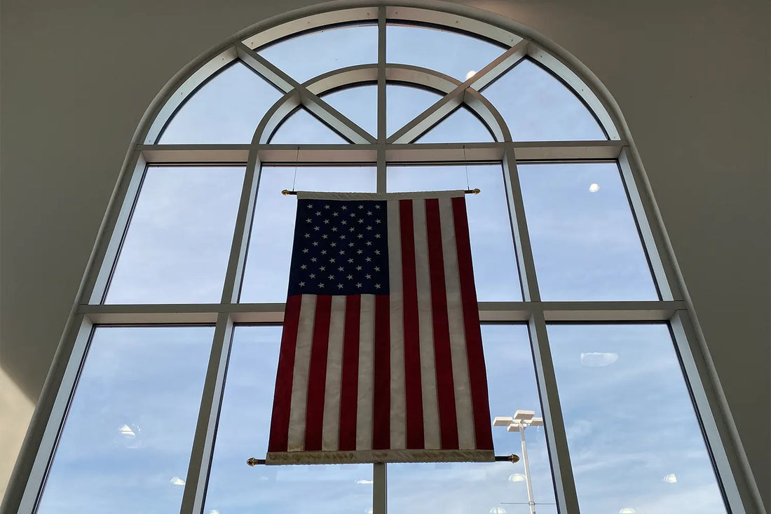 United States flag hanging vertically in the center of a large window.